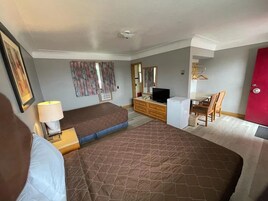 A hotel room with a bed, a desk with a computer, a chair, a wardrobe, and a red door.