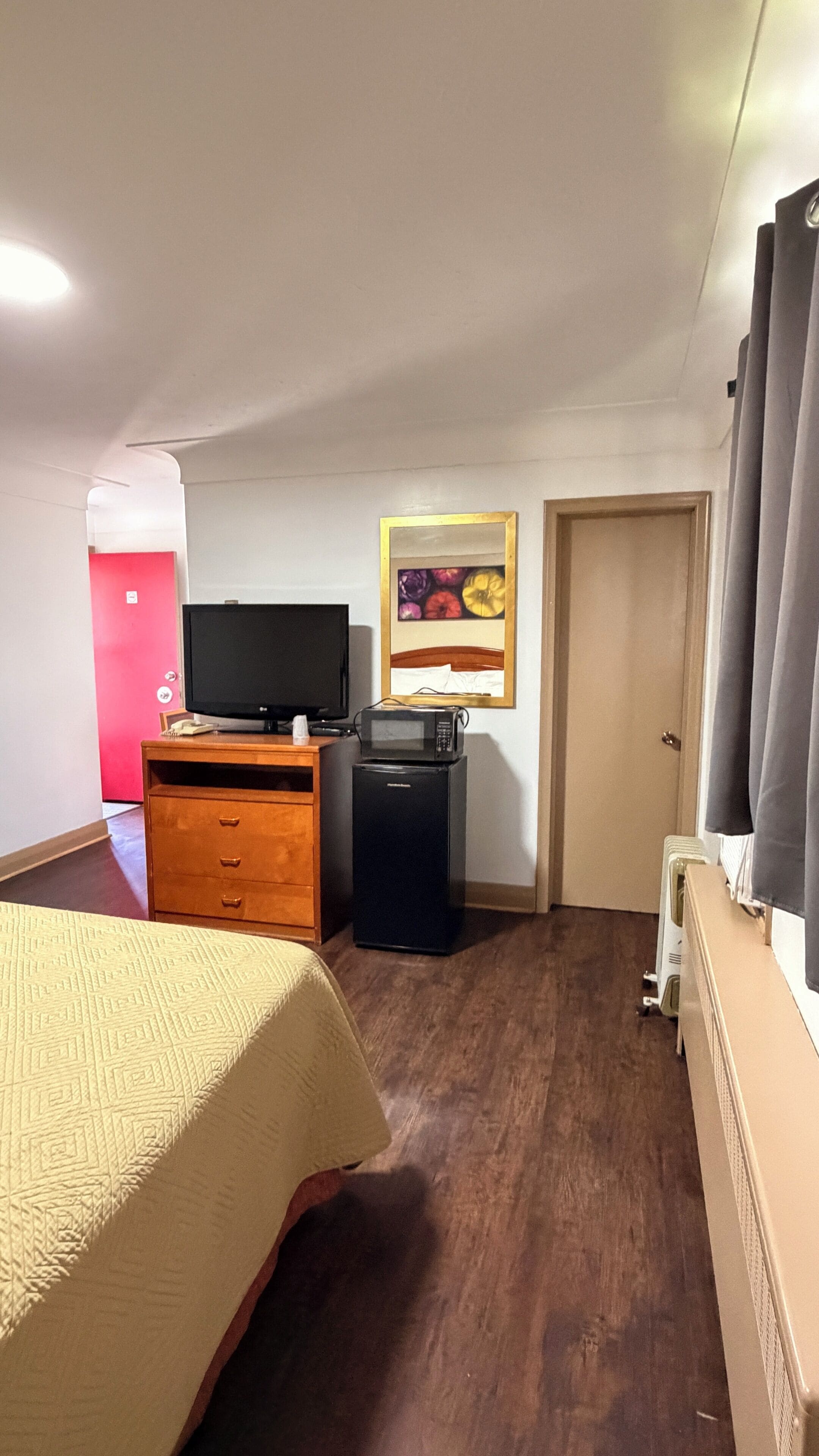 Ein Hotelzimmer mit einem Bett, einem Holzschrank, einem Fernseher, einer Mikrowelle und einer Tür.
