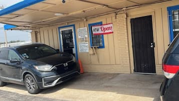 A building with a 'NEW OPEN' sign, a black car parked in front, and a blue awning.