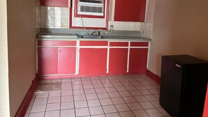 Une cuisine de taille réduite avec des meubles rouges, un crédence en carrelage blanc et un réfrigérateur noir.
