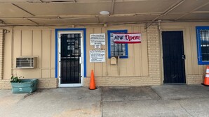 L’entrée d’un hôtel, avec un auvent bleu, une pancarte indiquant « Ouvert maintenant ! », une porte fermée et une caméra de surveillance.
