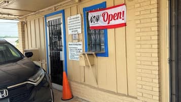A hotel entrance with a 'View Open!' sign, a check-in time of 12:00 noon, and a parking area with a car and a traffic cone.