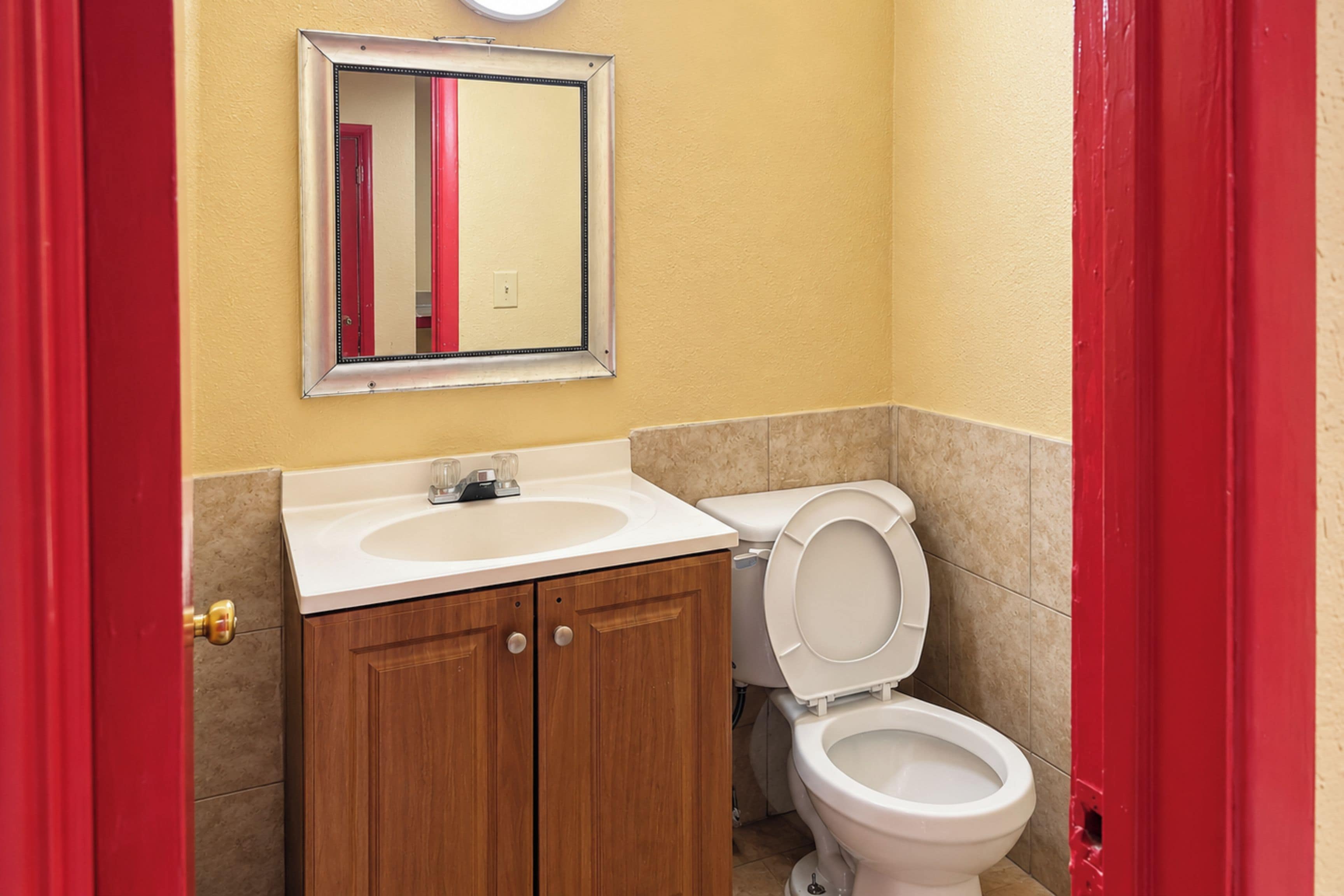A bathroom with a white sink, wooden cabinets, a toilet, and a mirror on the wall.