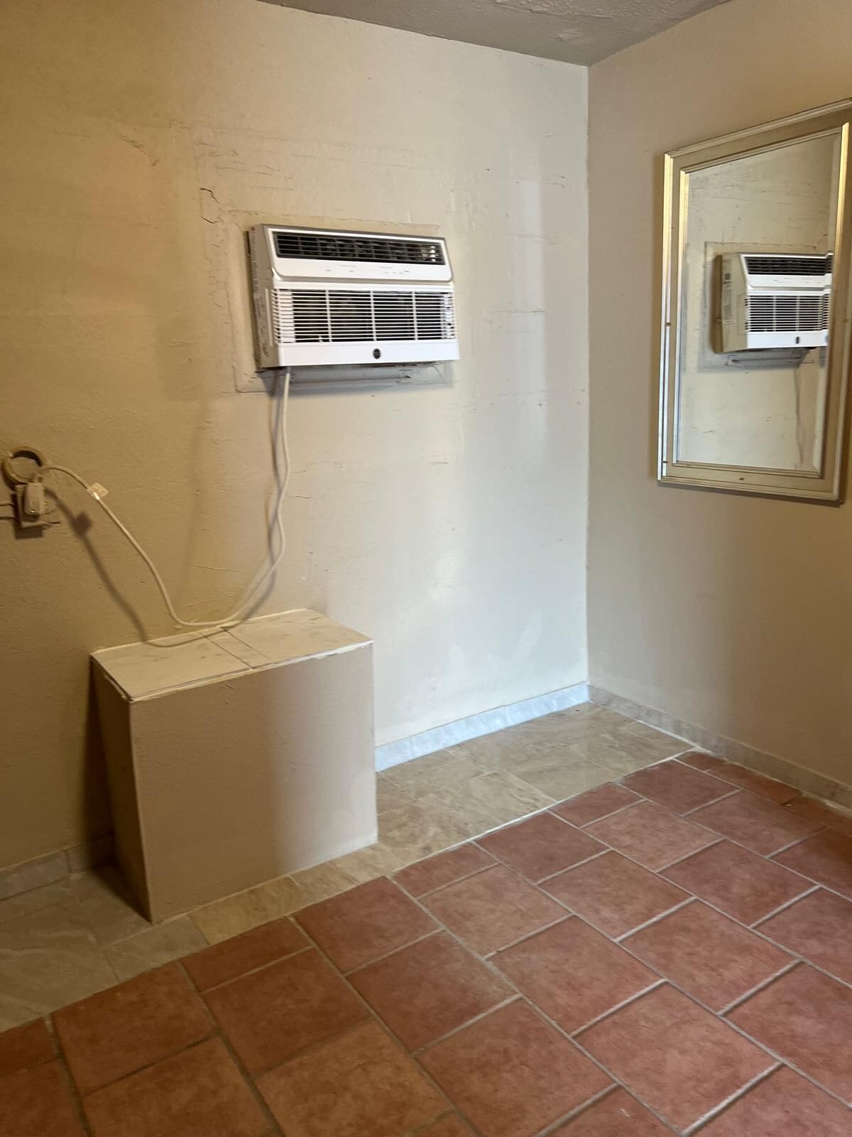 A bathroom with a white pedestal sink, a wall-mounted air conditioner, and a mirror with a wooden frame.