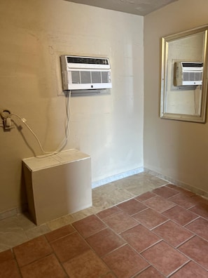 A bathroom with a white pedestal sink, a wall-mounted air conditioner, and a mirror with a wooden frame. - Holiday Motel Tulsa OK (Tulsa)