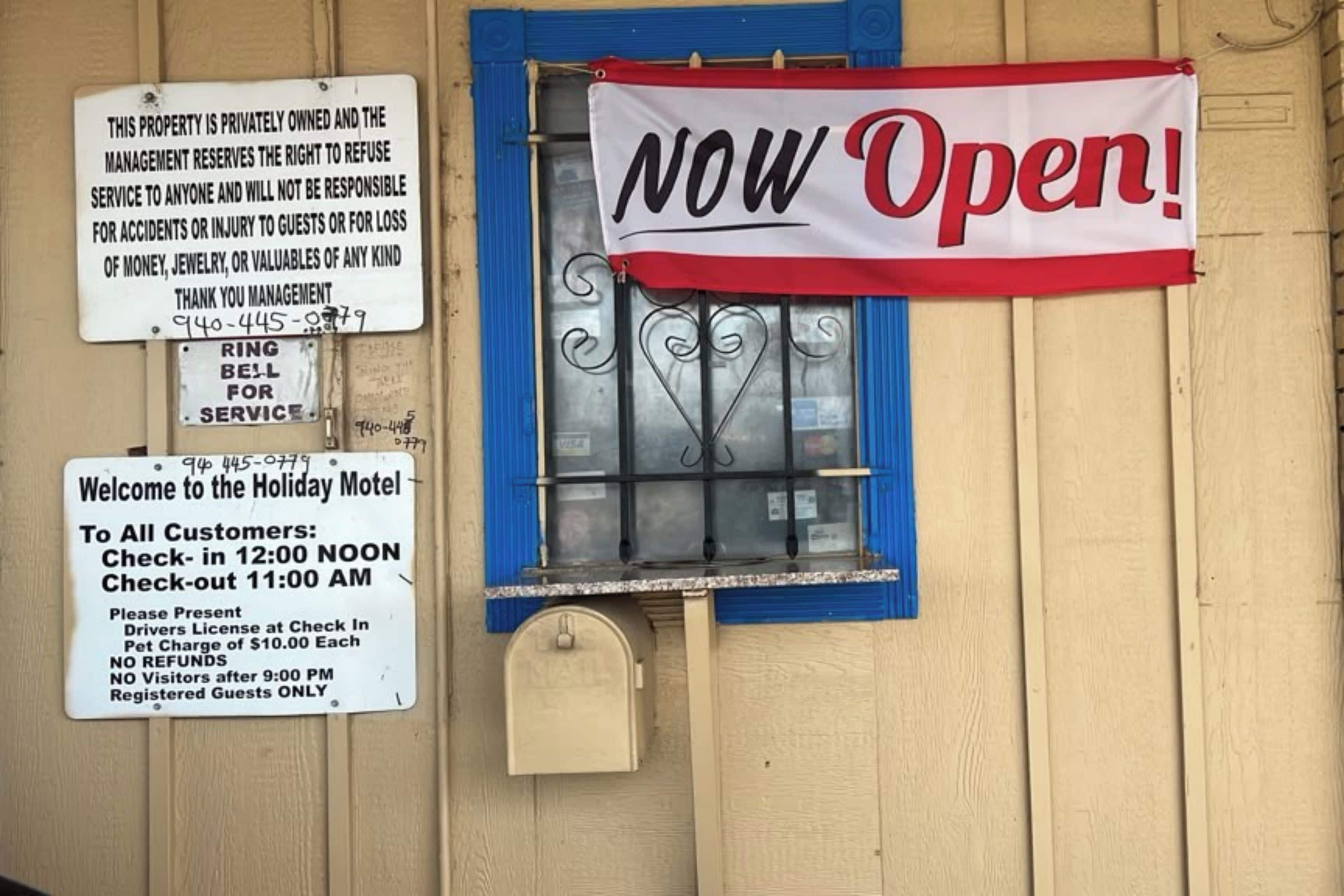 A motel sign with a 'NOW Open!' banner, a check-in/check-out schedule, and a notice about no refunds after 9:00 PM.