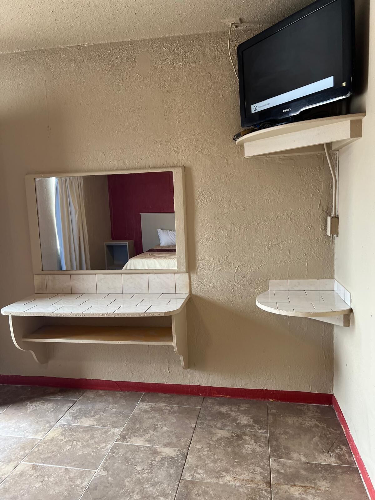 A room with a television mounted on a wall, a mirror, and a small shelf.