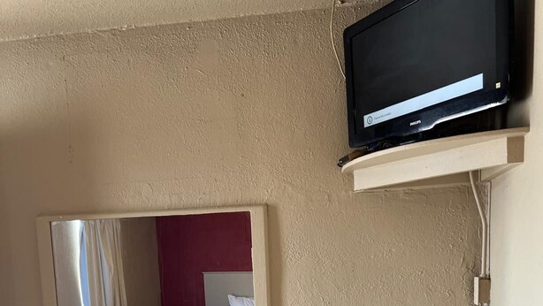 Une pièce avec un téléviseur fixé au mur, un miroir et une petite étagère.