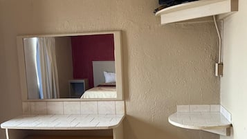 A room with a television mounted on a wall, a mirror, and a small shelf.
