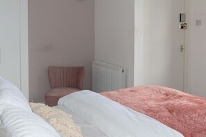 A bedroom with two beds, one with white bedding and the other with pink bedding, a pink chair, and a white radiator. - Studio Flat near University of Aberdeen (Aberdeen)
