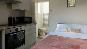 Ein kleines Schlafzimmer mit einem Bett, einem Nachttisch und Blick ins Bad.
