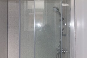 A shower enclosure with a glass door, a handheld showerhead, and a hose.