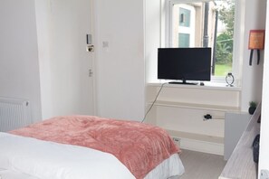 Un dormitorio con cama, televisión sobre un mueble, ventana y puerta.
