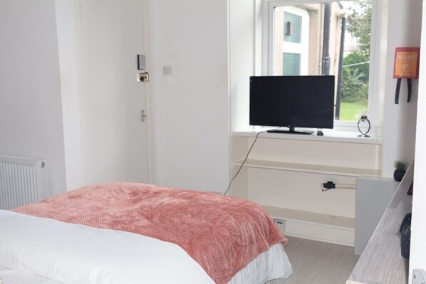 A bedroom with a bed, a television on a stand, a window, and a door.