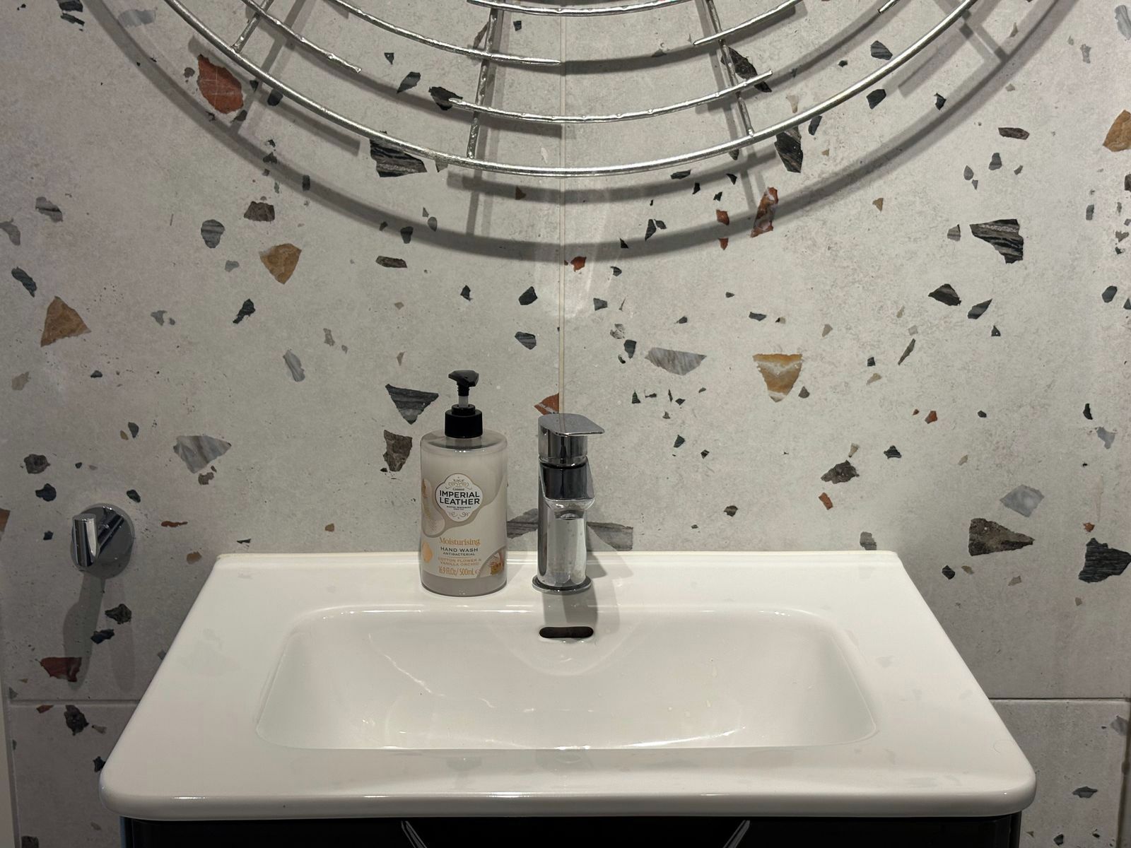 Ein Badezimmer mit einem weißen Waschbecken, einer Seifenspender und einem Spiegel mit Metallrahmen.