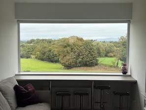 A room with a large window overlooking a green landscape with trees and a field.