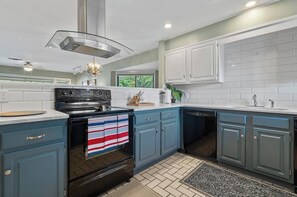 A modern kitchen with a black stove, blue cabinets, and a white tiled backsplash. - 2-bedroom condo in perfect Hot Springs with cool AC (Hot Springs)