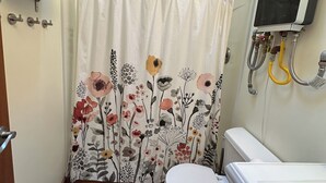 A small bathroom with a toilet, a shower curtain with floral patterns, a towel rack, and a water heater.
