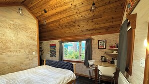 A wooden cabin room with a bed, a desk, and a window.