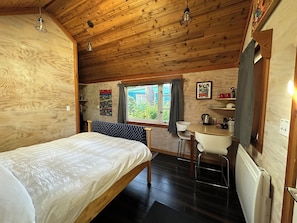 Ein Zimmer in einer Holzhütte mit einem Bett, einem Schreibtisch und einem Fenster.