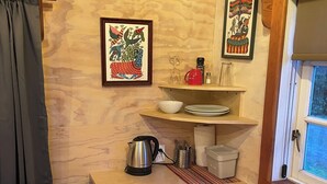 A small kitchen with a wooden table, two white chairs, a kettle, and two framed pictures on the wall.