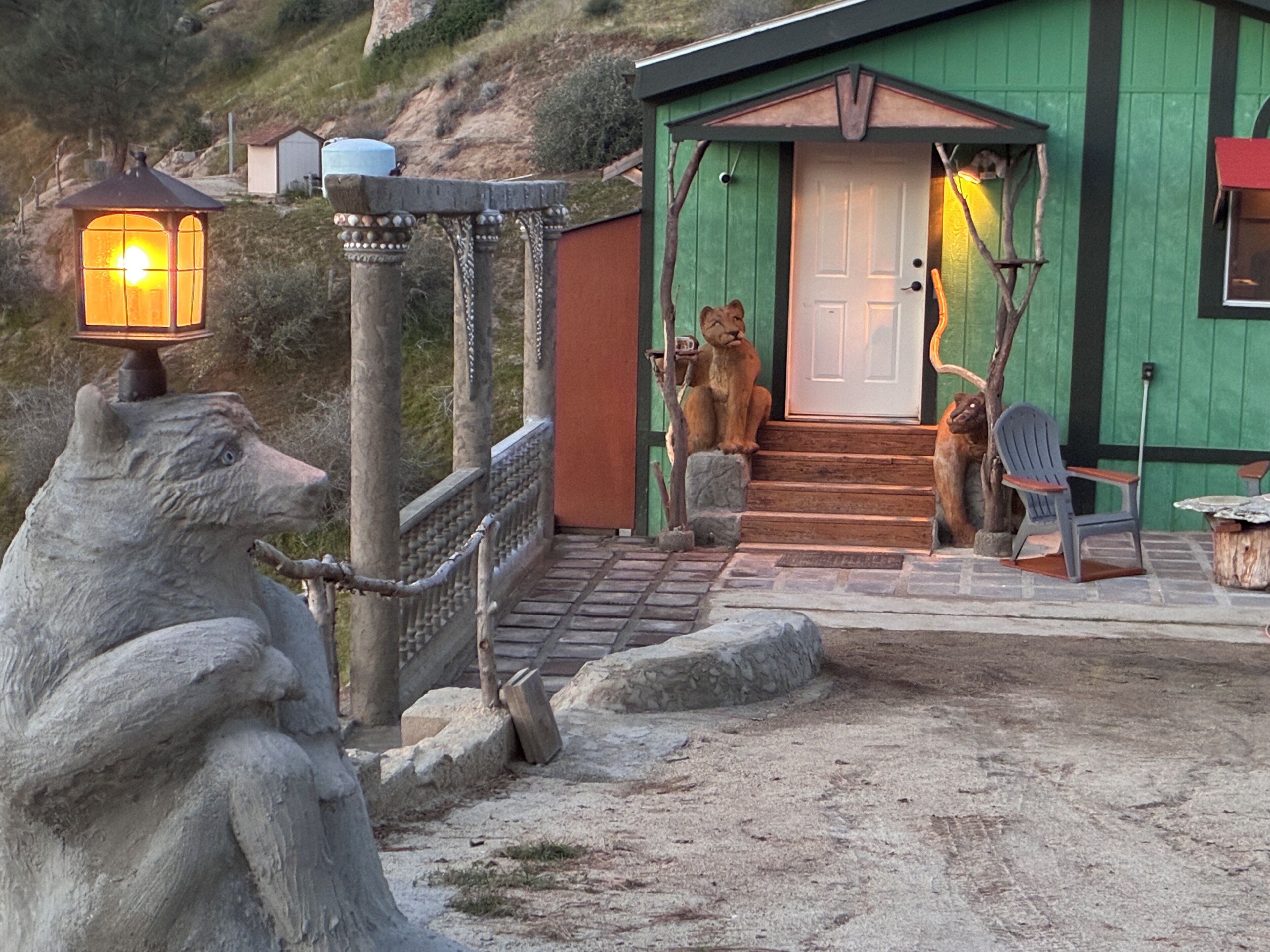 Eine rustikale Holzhütte mit grüner Fassade, einer Holzterrasse und einer Steinstatue eines Bären.
