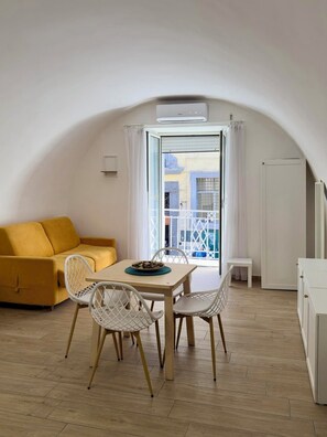 A dining area with a table and chairs, a yellow sofa, and a view through a window with a white curtain. - Your home in the heart of the Rione Sanità neighborhood. Authenticity, relaxation, and charm. (Napoli)