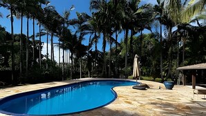 A swimming pool with a curved edge, surrounded by stone tiles and palm trees. - Casa Luxo Lagoa Piscina Jacuzzi Praia (São Francisco do Sul)