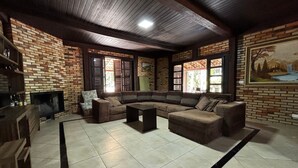 A living room with a brick wall, a large sectional sofa, a flat-screen TV, and a fireplace. - Casa Luxo Lagoa Piscina Jacuzzi Praia (São Francisco do Sul)