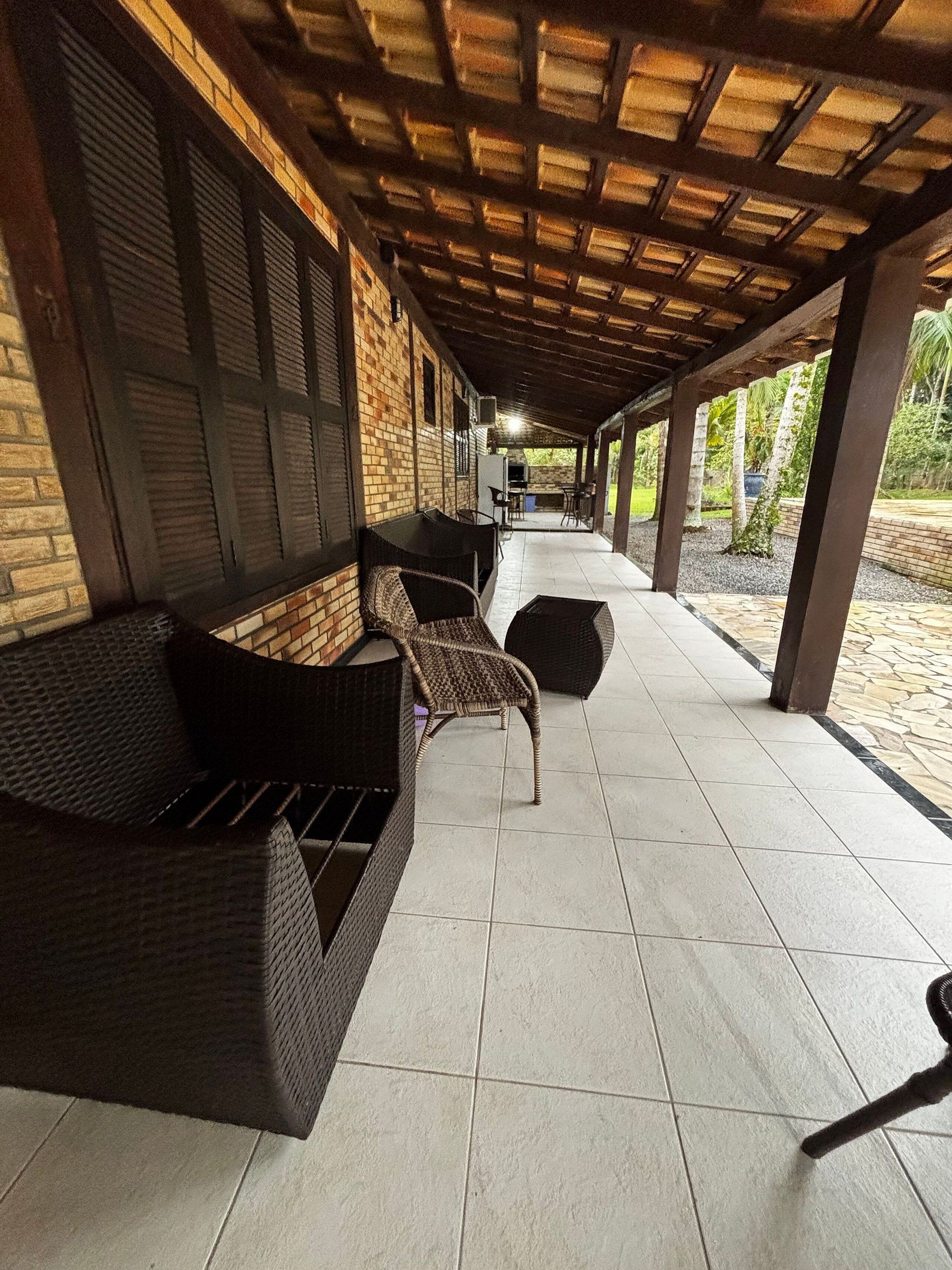 Un área de patio techada al aire libre con mobiliario de mimbre, piso de baldosas y pared de ladrillo.