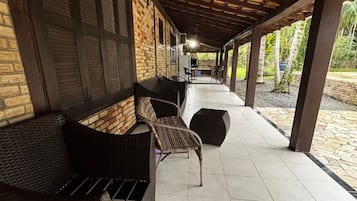 Un área de patio techada al aire libre con mobiliario de mimbre, piso de baldosas y pared de ladrillo.