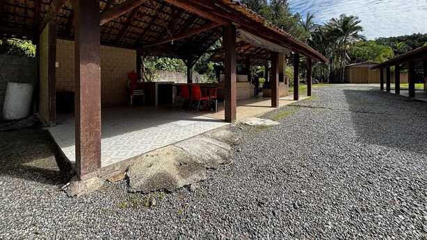 A covered outdoor seating area with red chairs, a table, and a brick wall. - Casa Luxo Lagoa Piscina Jacuzzi Praia (São Francisco do Sul)