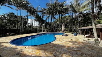 Una piscina con cubierta de piedra, rodeada de palmeras y una estructura de madera.