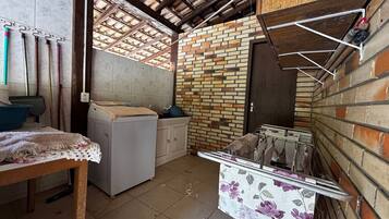 A compact kitchen with a brick wall, a washing machine, and a table with a floral tablecloth.