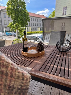 Ein Holztisch mit einer Weinflasche, Gläsern und einer Kiefernwalze auf einem Balkon mit Blick auf eine Stadtlandschaft.