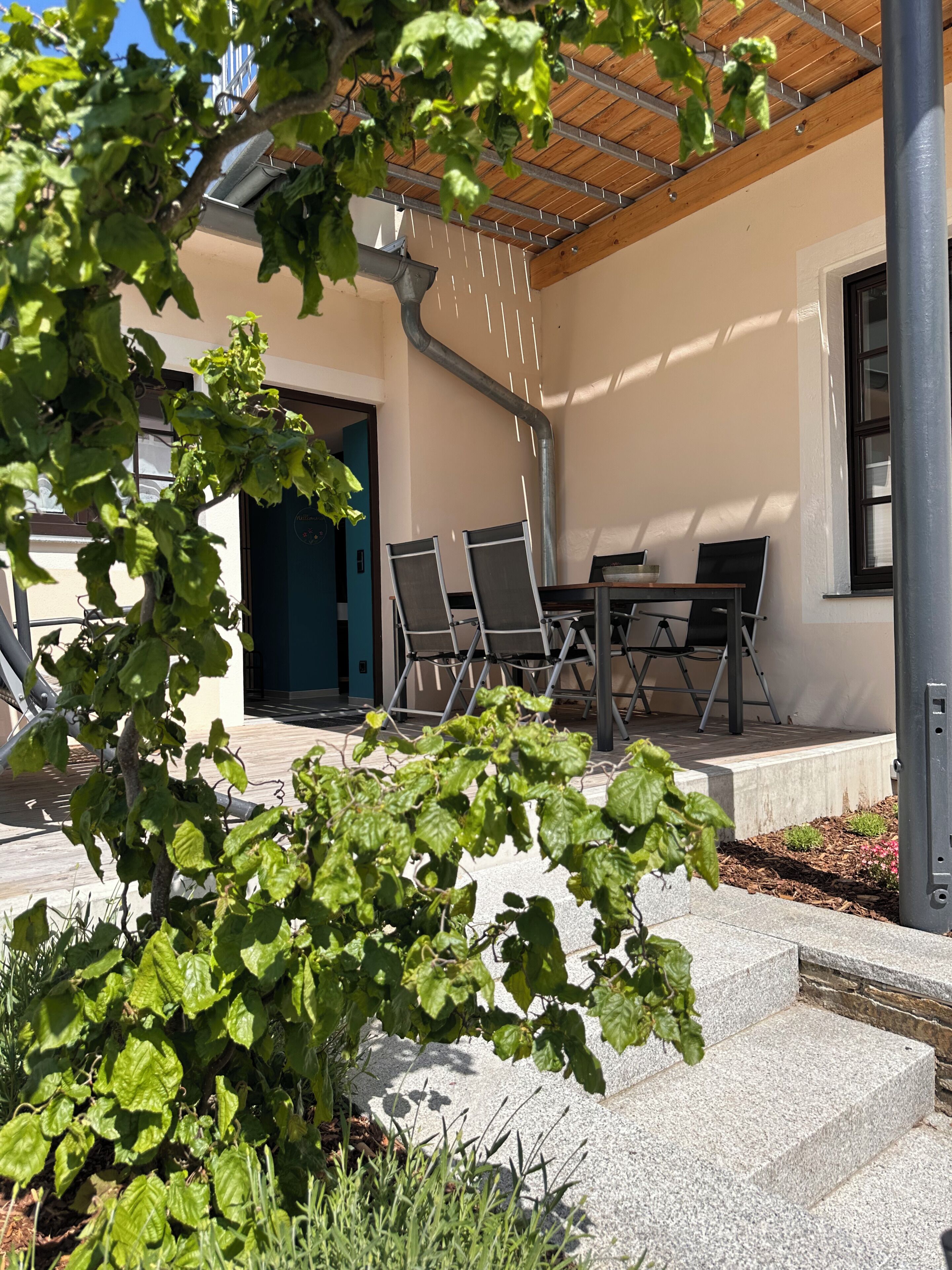An outdoor patio with a table and chairs, a covered area with a wooden ceiling, and a building entrance.