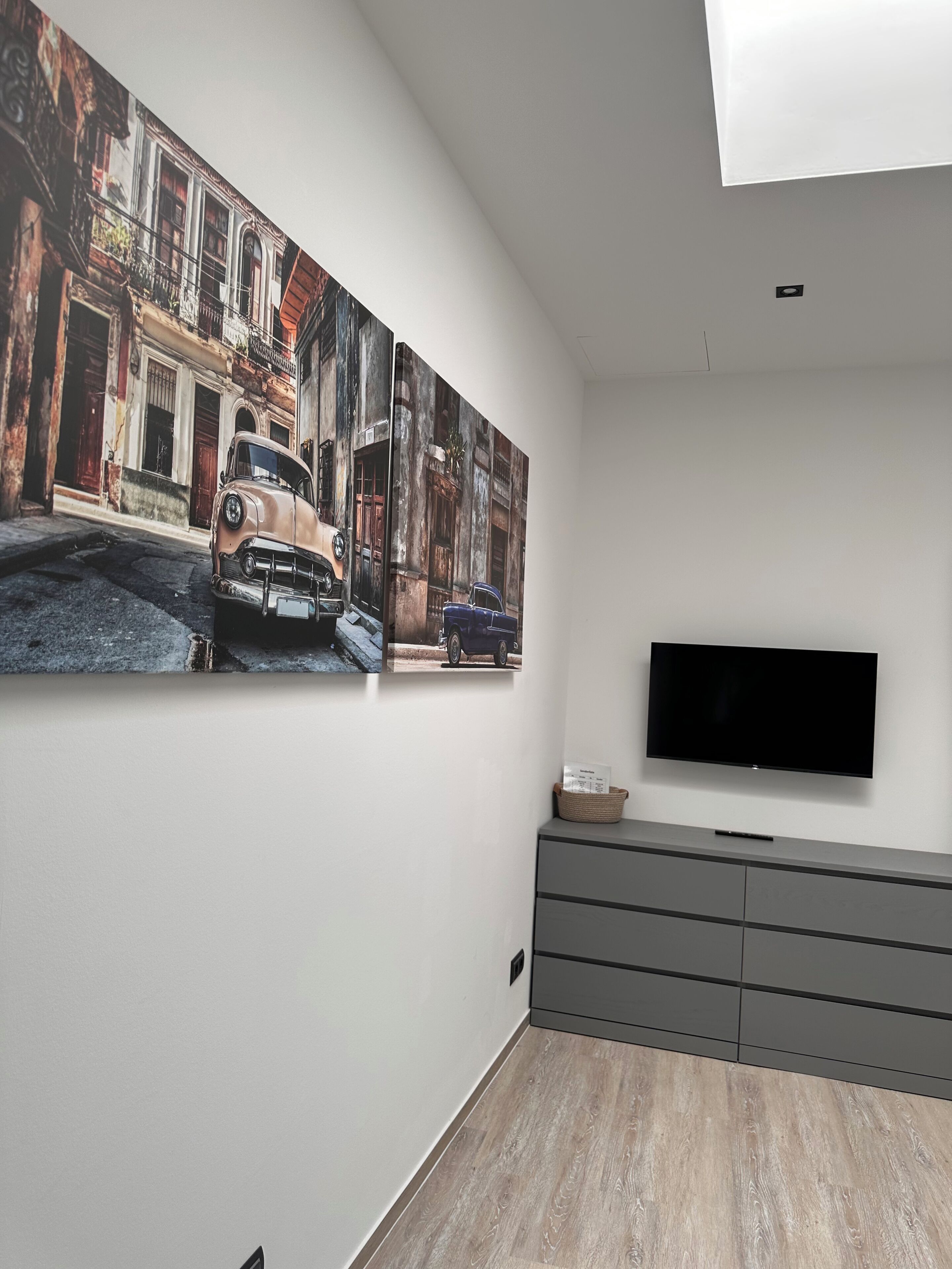 A modern living room with a large wall mural, a flat-screen TV, and a grey cabinet.