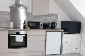 A compact kitchen with a built-in oven, microwave, coffee maker, and a small refrigerator.
