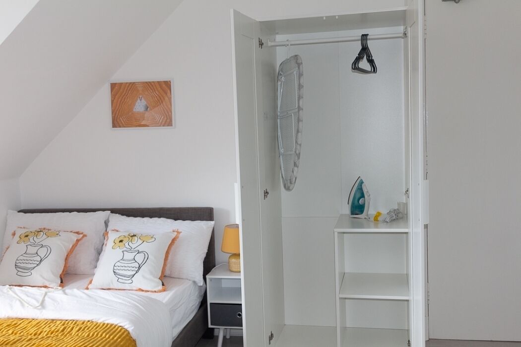 A bedroom with a bed, pillows, a nightstand, a lamp, a wardrobe, and a shower curtain.
