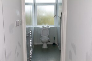 A bathroom with a toilet, a window, and a broom.