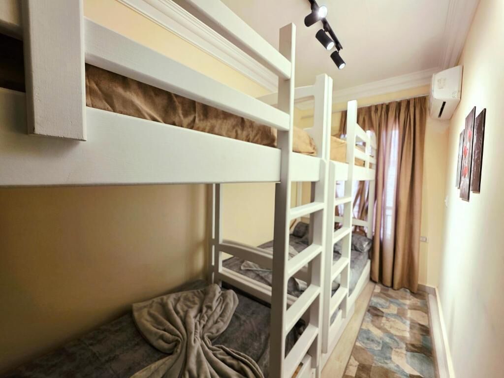 Ein Schlafraum mit Etagenbett, Kopfteil, kleinem Tisch und Vorhang.