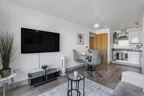 A modern living room with a flat-screen TV, a dining area with chairs, a kitchen with appliances, and a large potted plant. - Central Apt - Balcony | Netflix | Walk to Bullring (Birmingham)