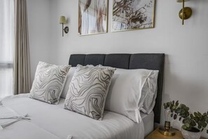 A neatly made bed with a dark headboard, two patterned pillows, and a bedside table with a lamp and a plant. - Central Apt - Balcony | Netflix | Walk to Bullring (Birmingham)