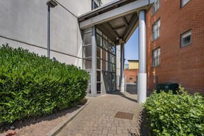 A pathway leading to a building with a covered entrance, a brick wall, and a green hedge. - Central Apt - Balcony | Netflix | Walk to Bullring (Birmingham)