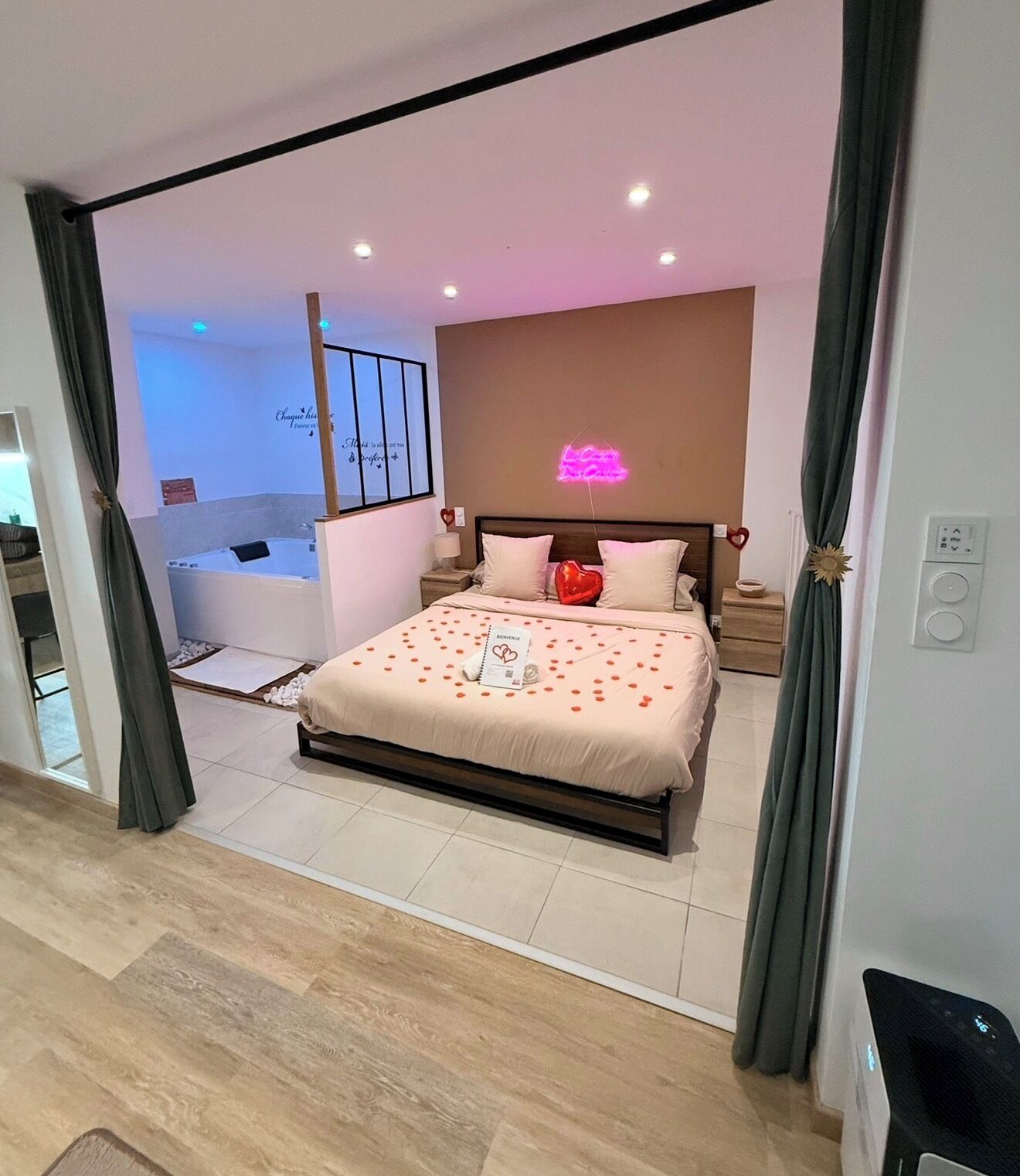A modern bedroom with a bed, bedside tables, a neon sign, and a view of a bathroom.