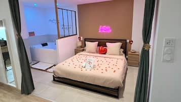 A modern bedroom with a bed, bedside tables, a neon sign, and a view of a bathroom.