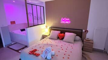 A hotel room with a bed, bedside tables, a nightstand, a wall-mounted lamp, and a neon sign.