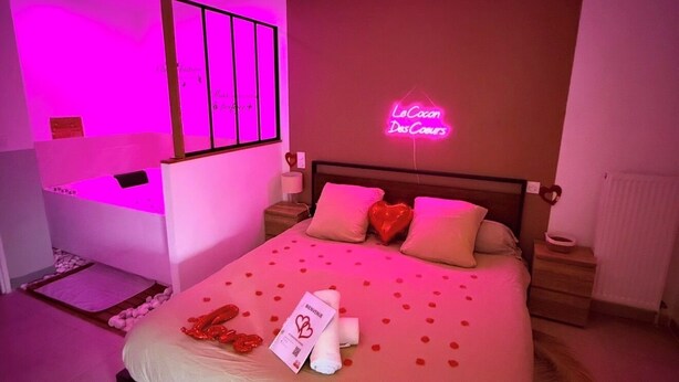 Una habitación de hotel con una cama, un letrero de neón y una mesita de noche.