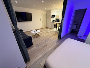 Een moderne hotelkamer met een bed, een ronde tafel, een bank, een televisie en een kitchenette.