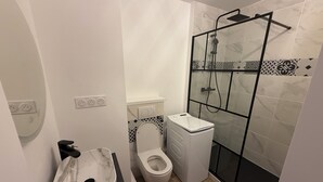Un baño con inodoro, cabina de ducha y lavadora.